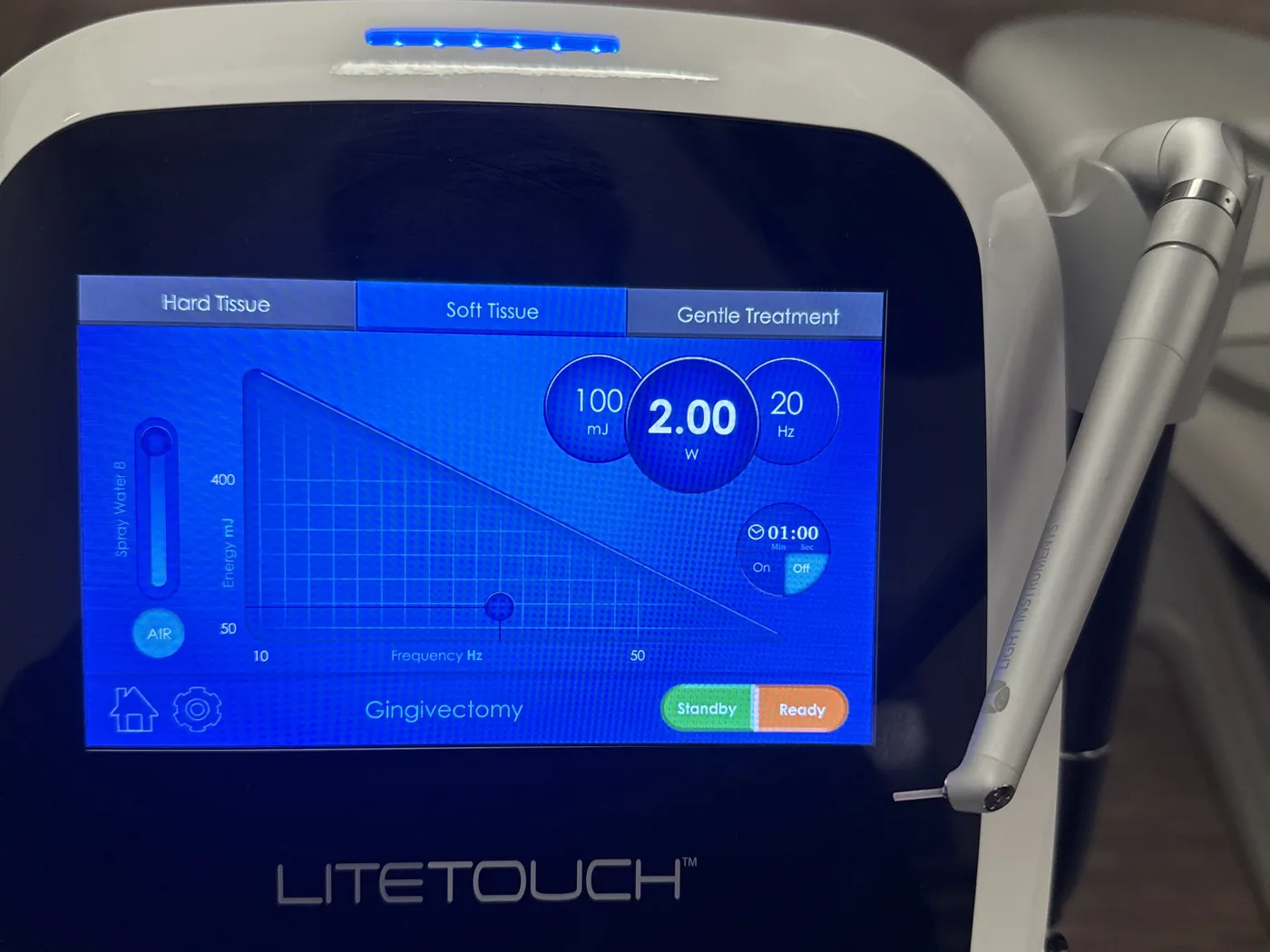 Control panel of the LiteTouch Er:YAG dental laser showing hard tissue and soft tissue modes, with the laser handpiece alongside